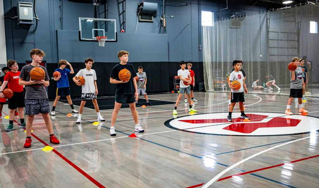 youth mens basketball players standing with basketballs behind cones
