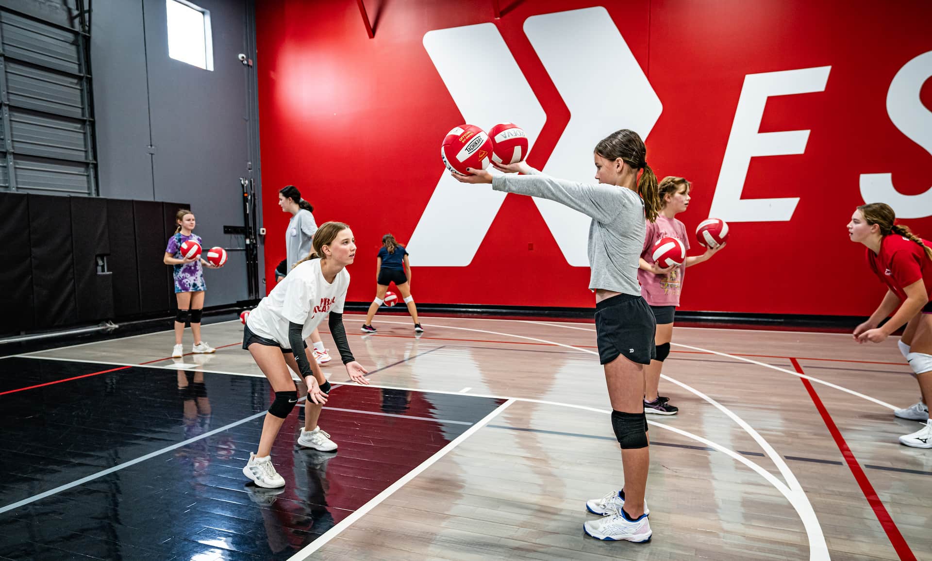 womens volleyball players stand holding volleyballs in partner drill